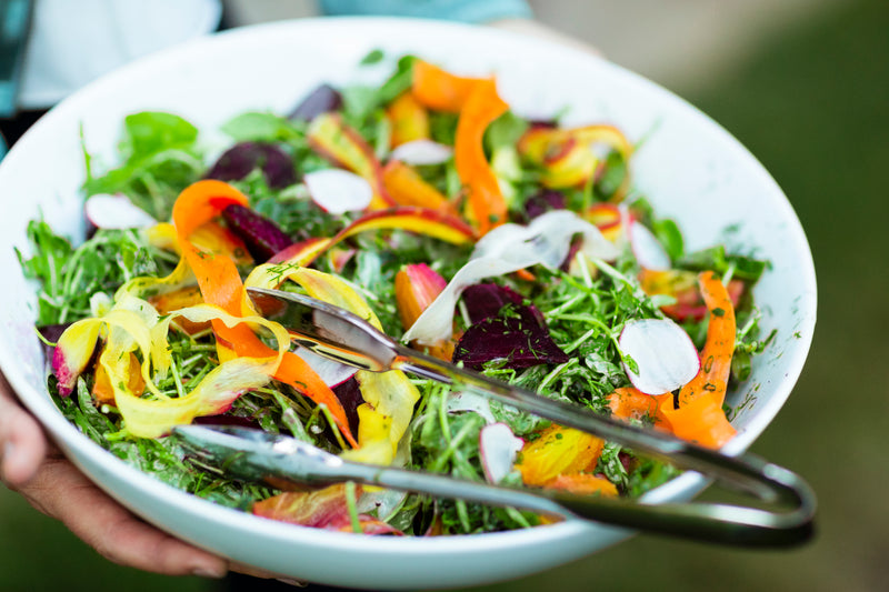 Colorful salad in a white bowl with tongs, held by a person.