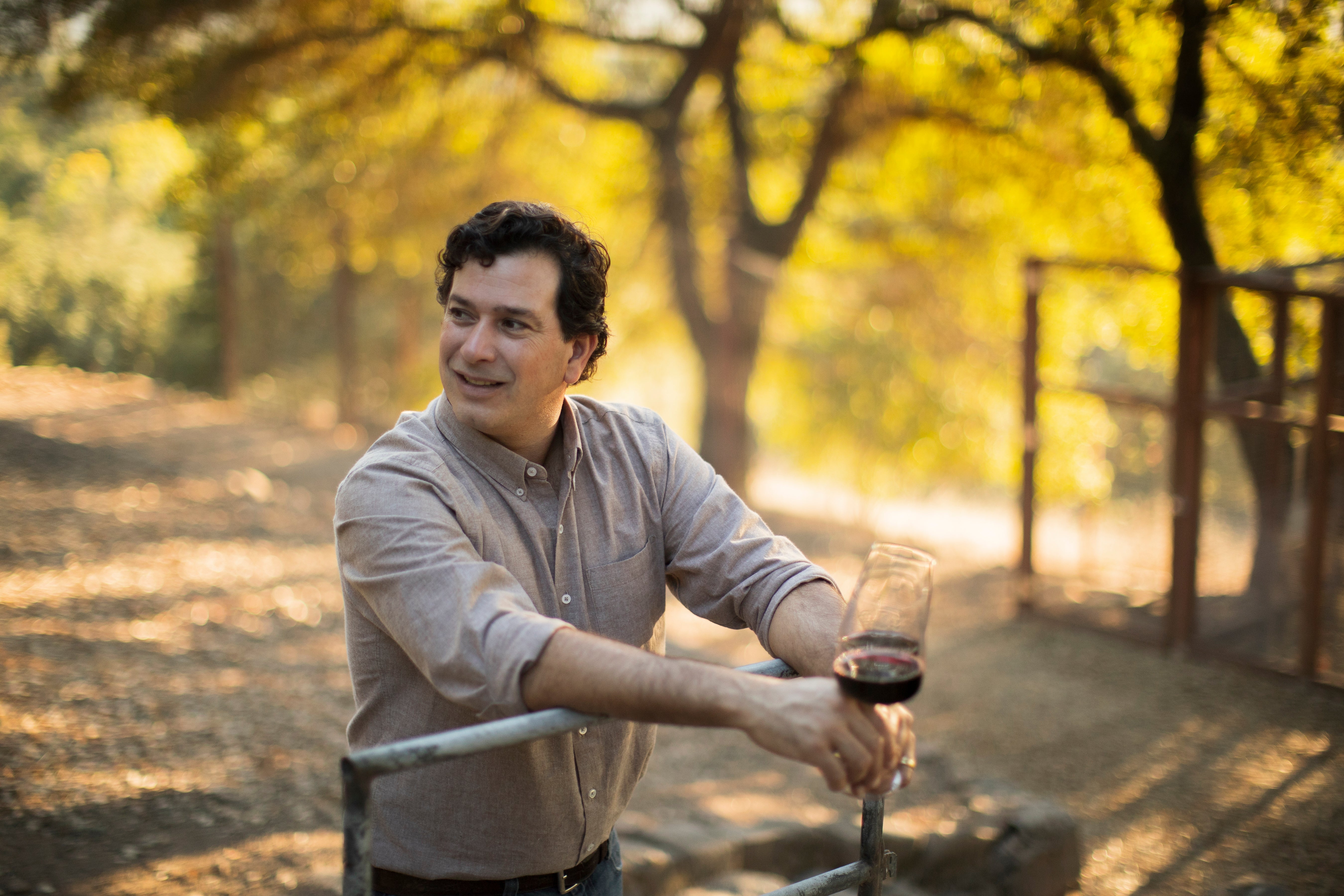 Man holding a glass of red wine in a vineyard setting