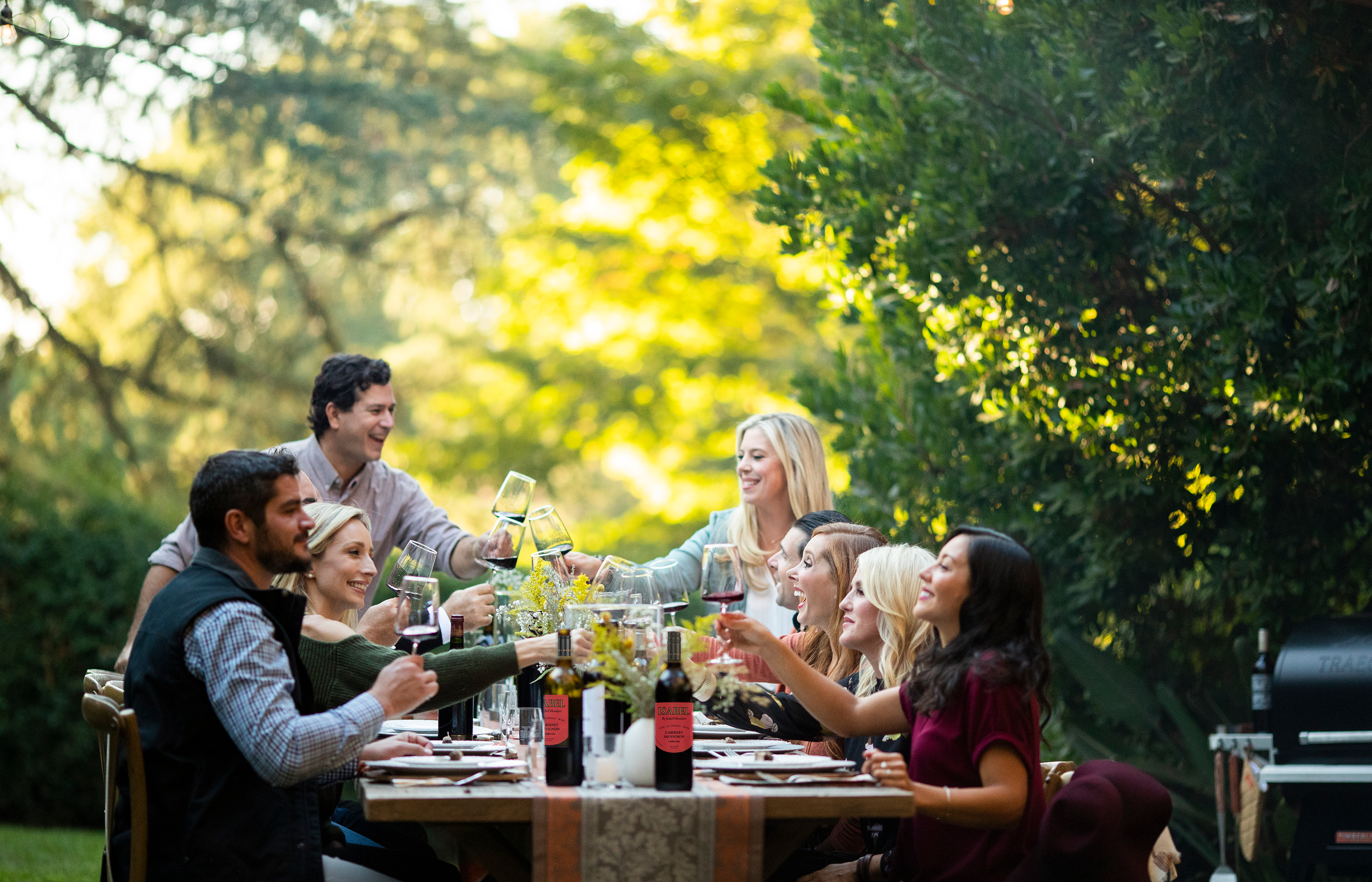 Group of people enjoying a meal and non-alcoholic wine outdoors with trees in the background