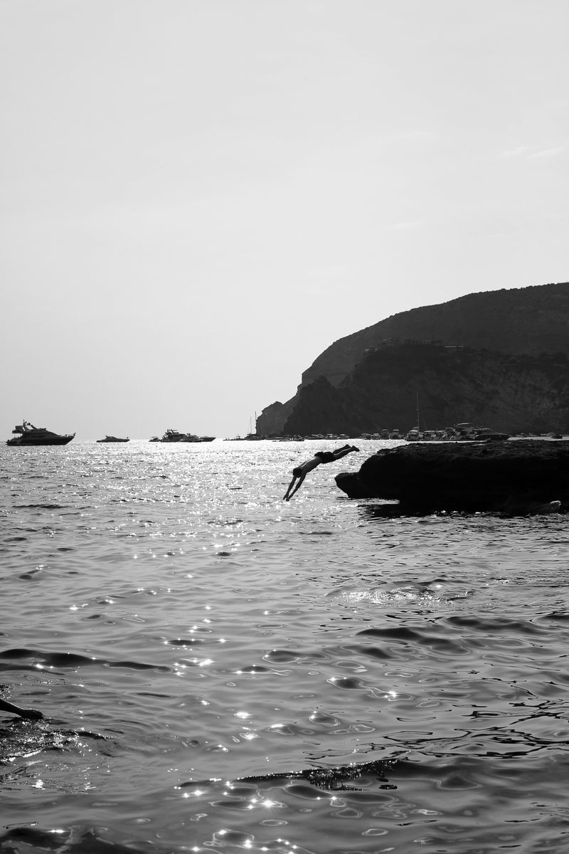 Person diving into the water from a rocky outcrop with a cliff in the background - la dolce vita lifestyle