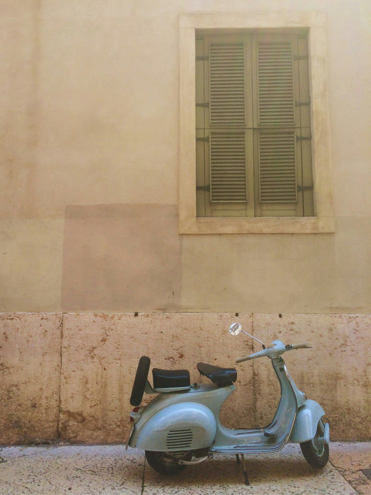 Vintage scooter parked against a beige wall with a window